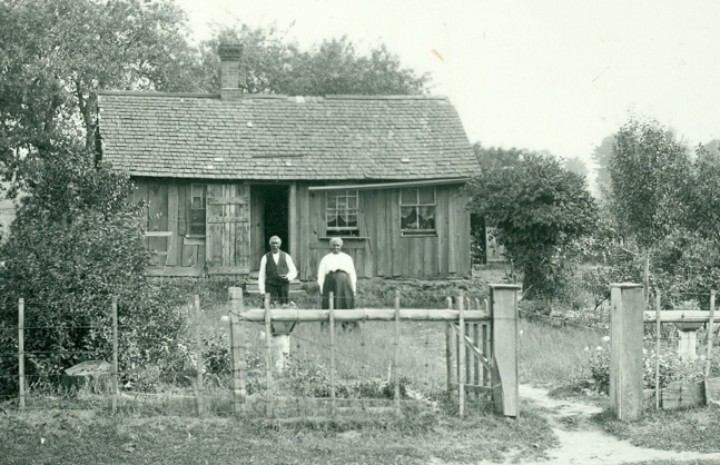 woman and man standing outside a wooden house black and white photo