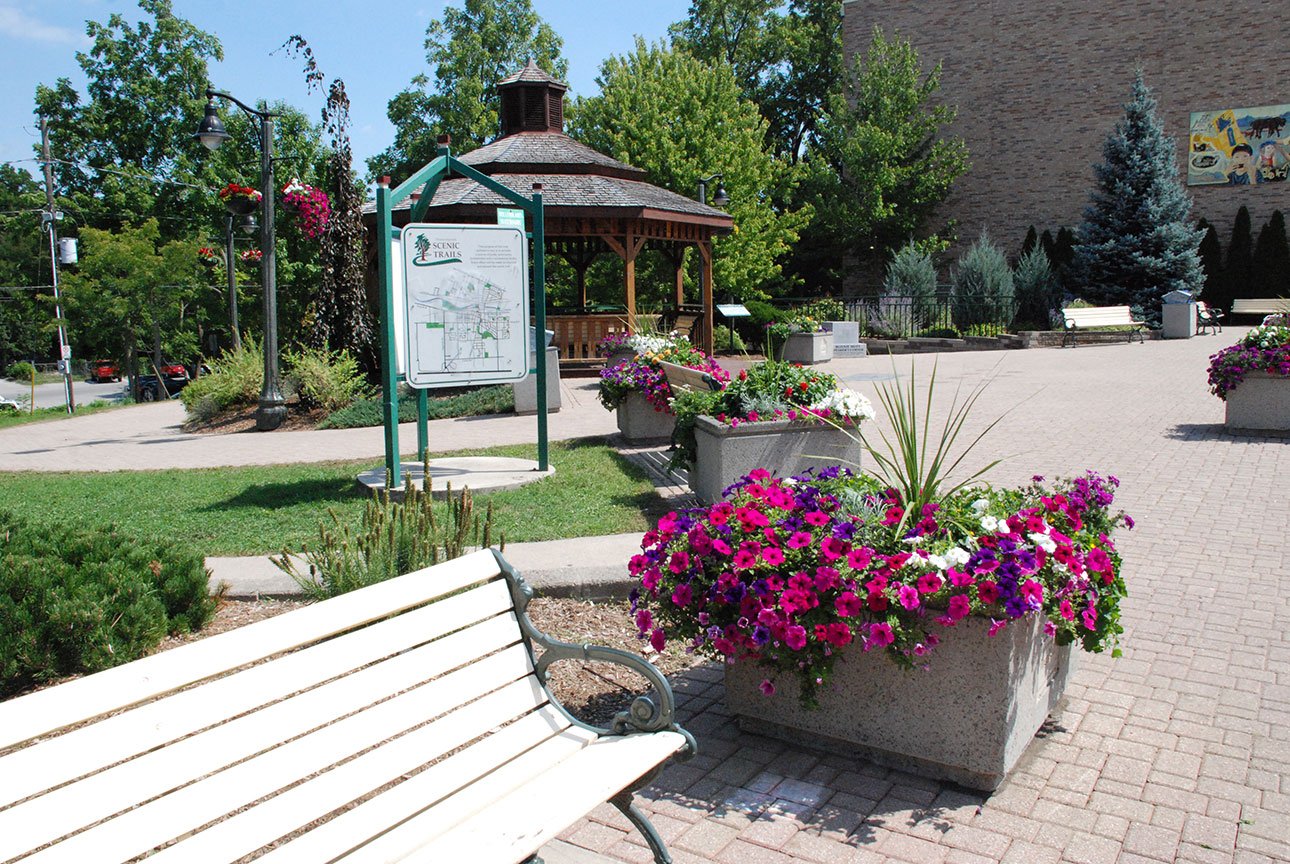 small town park with benches and flower pots, a sign showing a map of the town and a gazebo.