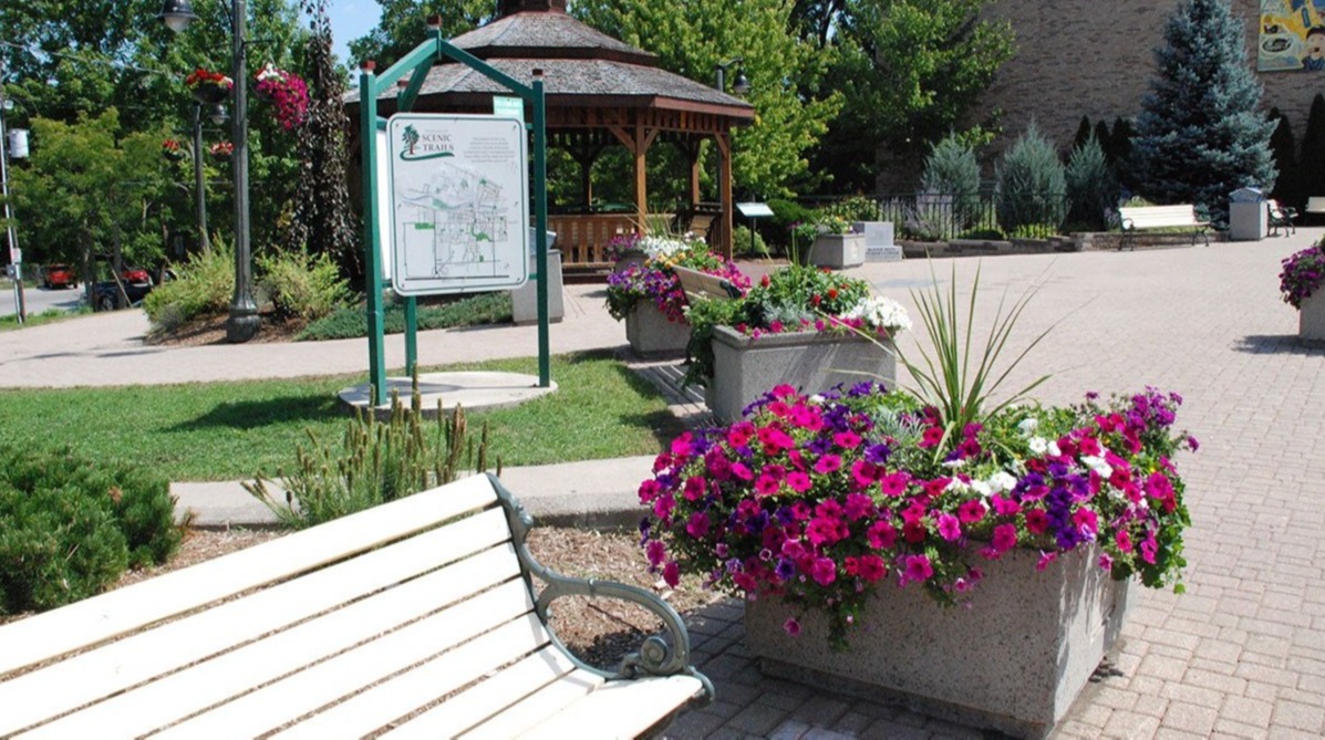 bench in the town centre with flower, grass, an information sign as well as a gazebo in the background