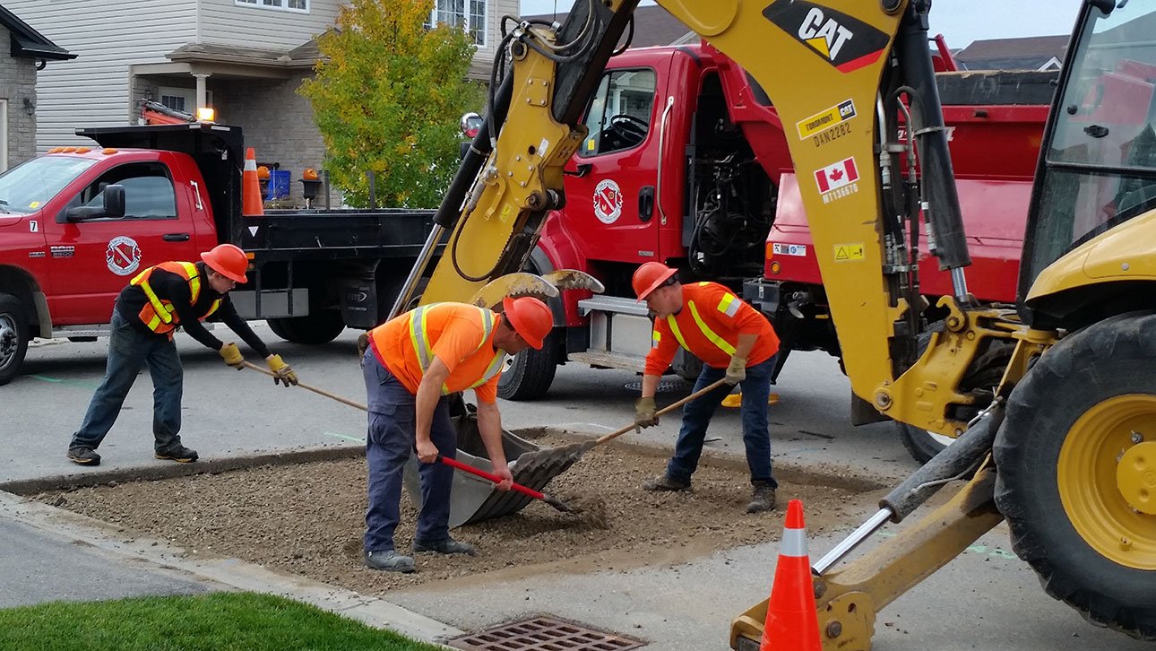 3 men working to fill potholes on the street with ash fault